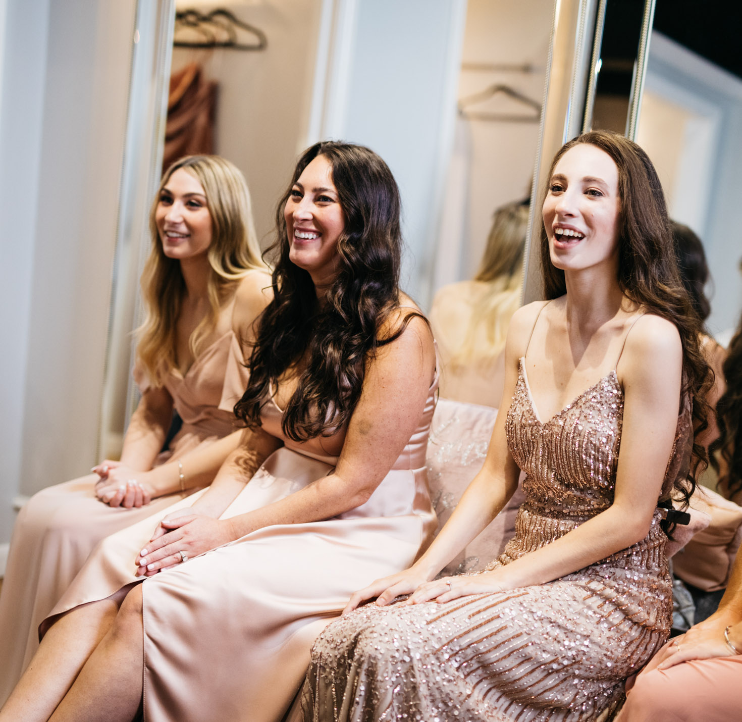 A bridal party watching others try on dresses and laughing.